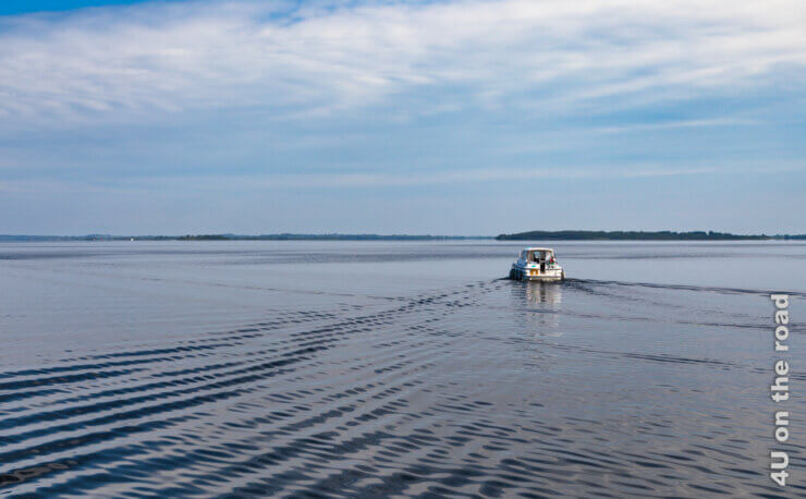 Ein grosser See, sich kreuzende Wellen und vom Wind geformte Wellen und ein Hausboot, am Horizont ein Streifen Land in Sicht - Feature Bild Urlaub im Hausboot