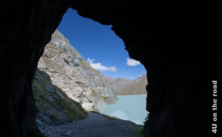 Das Feature Bild für den Beitrag zum Engerie tanken in den Alpen an der Staumauer Grand Dixence zeigt aus eine Tunnel heraus den Lac des Dix und die Staumer in der schönen Bergwelt
